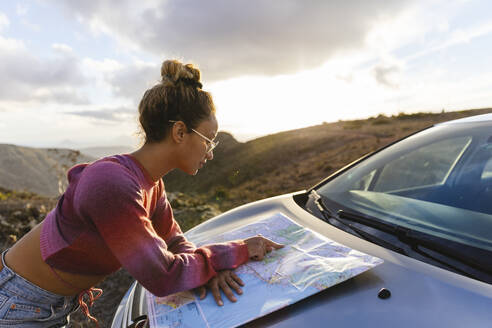 Frau zeigt auf Karte, die auf der Motorhaube eines Autos liegt - MRAF00822