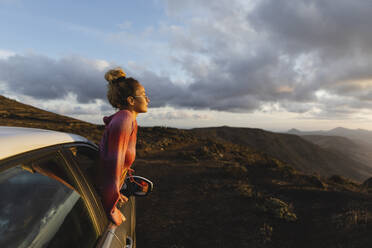 Young woman leaning out of car window looking at mountain landscape - MRAF00832