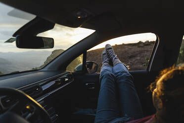 Young woman relaxing with feet up on car window at sunset - MRAF00834