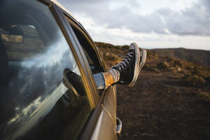 Frau mit hochgelegten Füßen am Autofenster bei Sonnenuntergang - MRAF00837