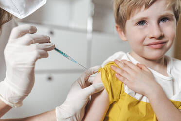 Krankenschwester mit Schutzhandschuh und Maske beim Impfen eines Jungen im Zentrum - MFF08355