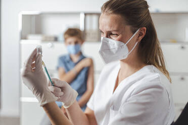 Doctor with protective face mask preparing vaccine injection at center - MFF08356