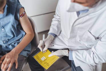 Doctor filling immunization certificate with boy at vaccination center - MFF08365