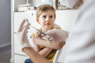 Boy looking at doctor preparing COVID-19 vaccine injection in center - MFF08375