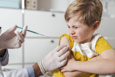 Doctor administering vaccination on arm of sceptical boy - MFF08383