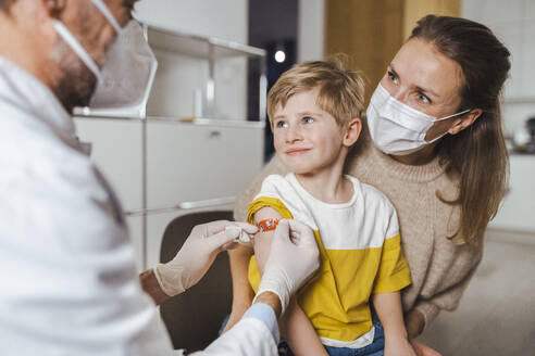 Doctor putting bandage on smiling boy's arm at center - MFF08389