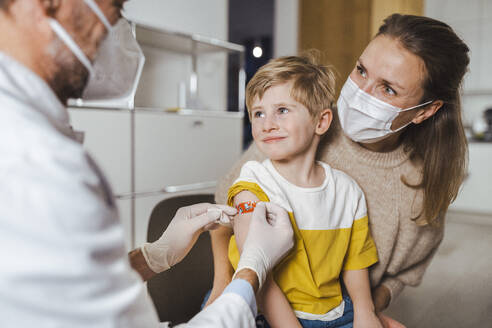 Ein Arzt legt einen Verband um den Arm eines lächelnden Jungen in der Mitte - MFF08389