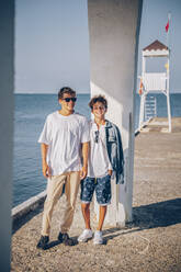 Smiling brothers standing on pier in front of sea - OMIF00312