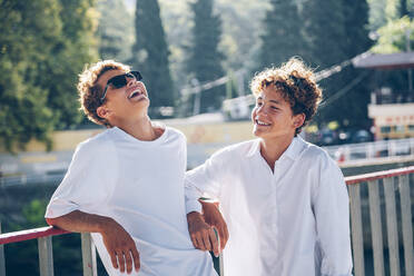 Cheerful siblings talking at bridge on sunny day - OMIF00319