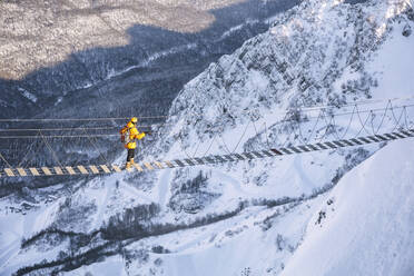 Mann wandert auf einer Seilbrücke über einen schneebedeckten Berg - OMIF00326