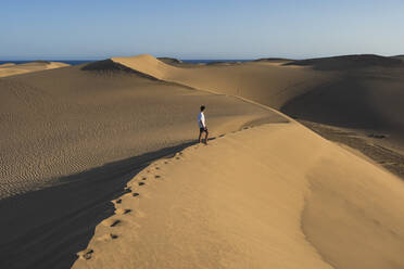 Junger Mann, der bei Sonnenuntergang auf einer Sanddüne spazieren geht, Gran Canaria, Kanarische Inseln, Spanien - RSGF00772
