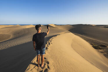 Mann nimmt Selfie durch Smartphone stehend auf Sanddüne, Grand Canary, Kanarische Inseln, Spanien - RSGF00774