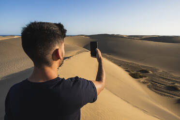 Tourist nimmt Selfie durch Smartphone in Wüste bei Sonnenuntergang, Grand Canary, Kanarische Inseln, Spanien - RSGF00775