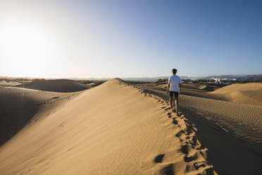 Junger Mann, der bei Sonnenuntergang unter blauem Himmel im Sand spazieren geht, Gran Canaria, Kanarische Inseln, Spanien - RSGF00776