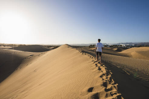 Junger Mann, der bei Sonnenuntergang unter blauem Himmel im Sand spazieren geht, Gran Canaria, Kanarische Inseln, Spanien - RSGF00776