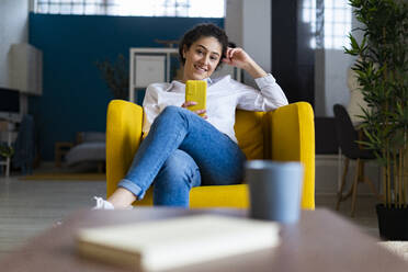 Lächelnde Frau mit Smartphone auf der Couch sitzend - GIOF14592