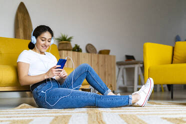 Young woman listening music using smart phone at home - GIOF14602