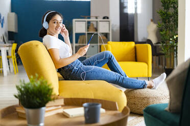 Junge Frau hört Musik und entspannt sich auf dem Sofa zu Hause - GIOF14605