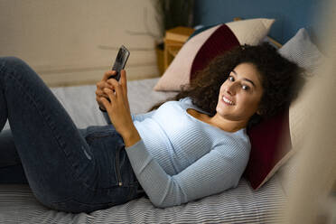 Frau mit Smartphone auf dem Bett liegend - GIOF14630