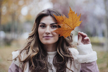 Young woman holding maple leaf at autumn park - EBBF05119