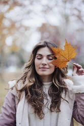 Woman holding maple leaf at autumn park - EBBF05120