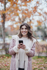 Junge Frau mit Smartphone im Herbstpark - EBBF05122