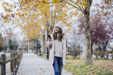 Smiling woman holding mobile phone on footpath - EBBF05129
