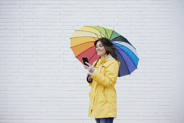 Frau mit Regenschirm und Mobiltelefon vor einer Mauer - EBBF05152