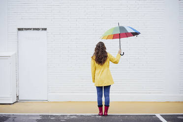Woman holding multi colored umbrella on footpath - EBBF05154