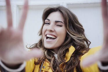 Happy woman with long brown hair winking in front of wall - EBBF05168