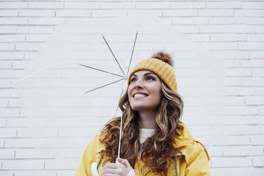 Smiling woman holding umbrella in front of wall - EBBF05174