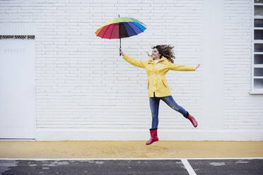 Glückliche Frau mit Regenschirm springt auf die Straße - EBBF05175