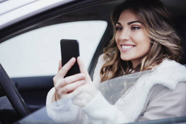 Smiling woman using mobile phone in car - EBBF05188