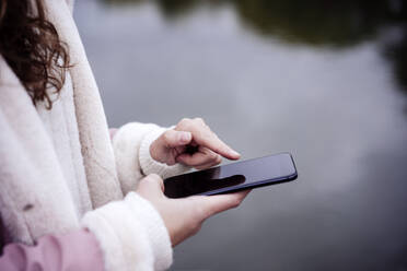 Woman using mobile phone at lakeside - EBBF05195
