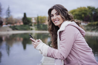 Smiling woman holding mobile phone on pier - EBBF05202