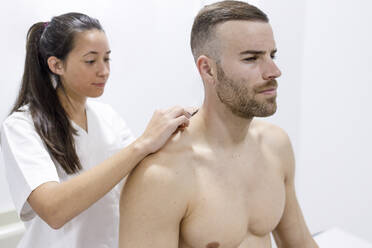 Physical therapist putting tape on shirtless athlete - IFRF01351