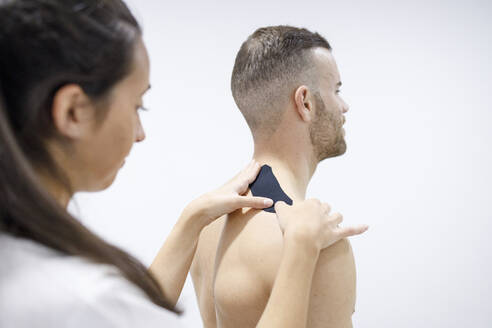 Physiotherapeutin klebt therapeutisches Band um die Schulter eines Sportlers - IFRF01353