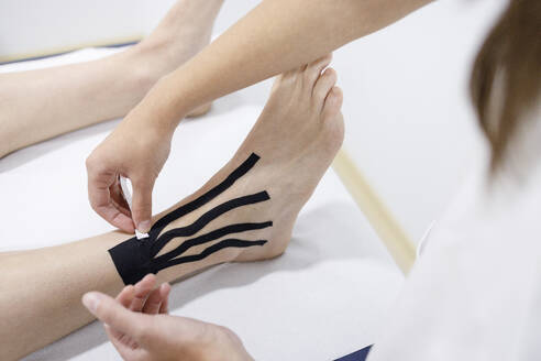 Physiotherapeutin klebt therapeutisches Band auf das Bein eines Sportlers am Massagetisch - IFRF01357