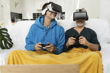 Gay couple playing video game through virtual reality headsets at home - JCCMF04866