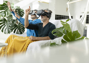 Gay couple using virtual reality headsets at home - JCCMF04867