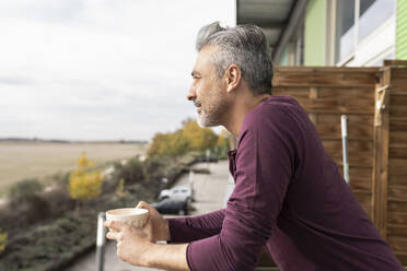 Man holding coffee cup at balcony - JCCMF04878