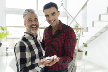 Happy gay couple holding new house key at home - JCCMF04896