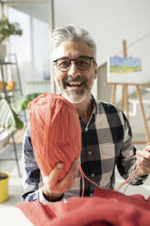 Smiling man with eyeglasses showing wool at home - JCCMF04906