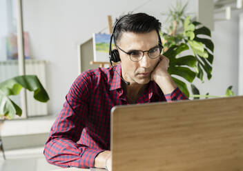 Businessman with headset using laptop at home - JCCMF04913
