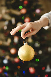 Woman holding bauble in front of christmas tree at home - EYAF01840