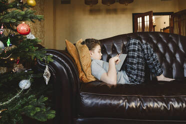 Boy using tablet PC lying on sofa at home - EYAF01841