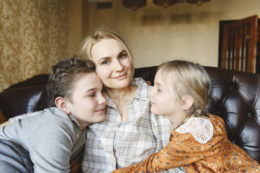 Smiling mother with daughter and son sitting on sofa at home - EYAF01842