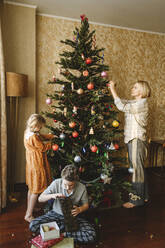 Familie schmückt Weihnachtsbaum zu Hause - EYAF01848