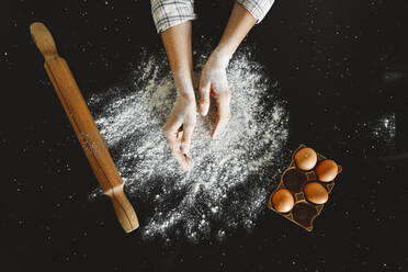 Frau beim Bestäuben von Mehl durch Eierkarton auf schwarzem Hintergrund - EYAF01858