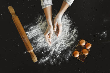 Woman dusting flour by egg tray on black background - EYAF01858